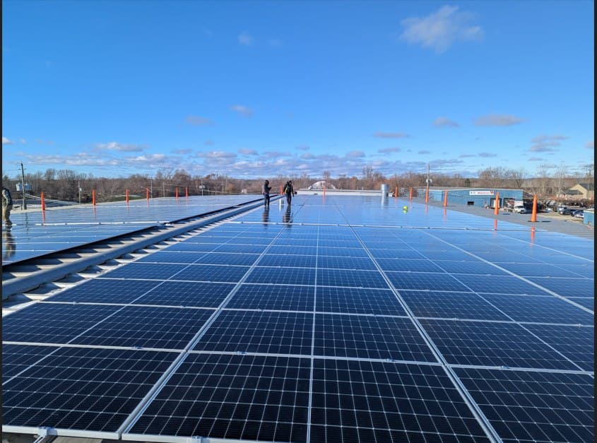 Two installers walking a large commercial rooftop solar array under a blue sky