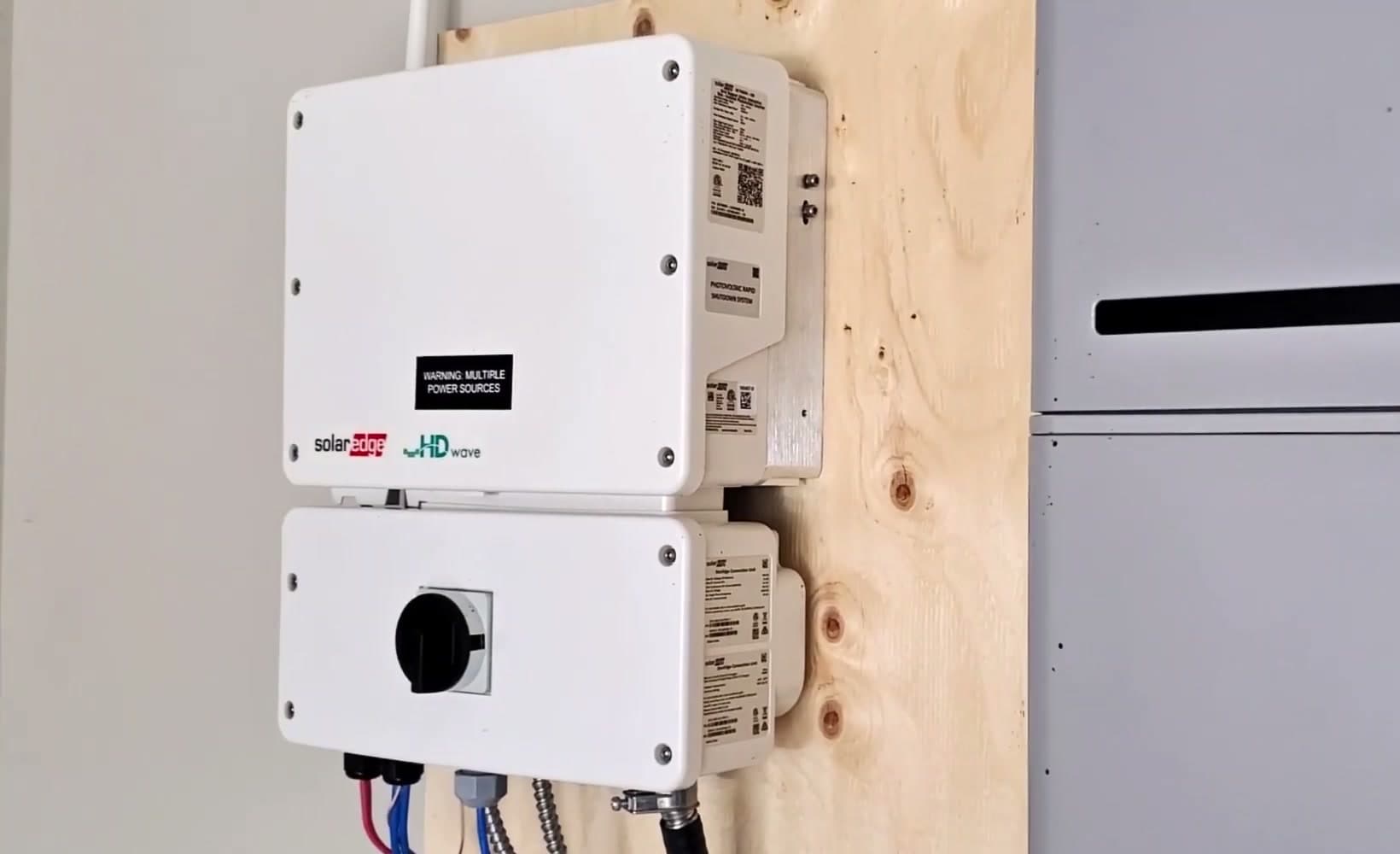 A solar inverter and a battery cabinet mounted on a plywood backboard