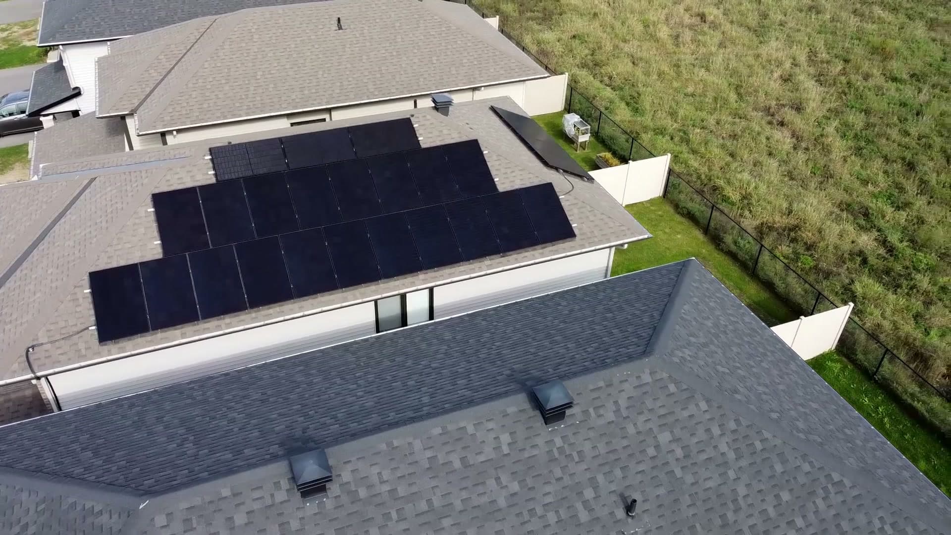 Black solar panels on a shingled roof in Orléans, seen from a drone