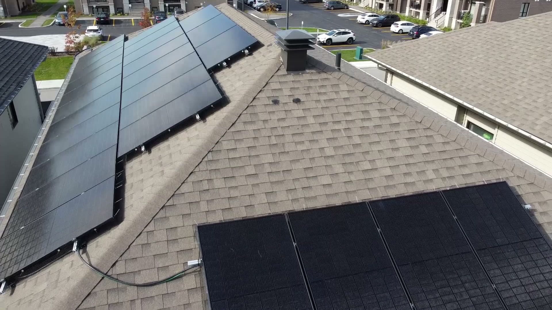 Black solar panels in rows on a shingled Orléans roof, seen from a drone